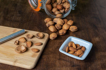 Jar with almonds next to some freshly split almond nuggets.