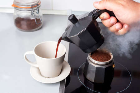 Disassembled coffee maker with one part on the fire and the other serving coffee in a cup.