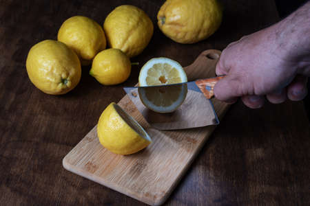 Cutting board next to some lemons, with a lemon cut in two halves by a huge knife.