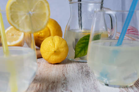 Lemon next to some glasses with straws and a pitcher of lemonade.