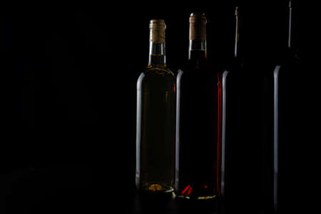 Several bottles of red, rosÃ© and white wine in a row and diminishing perspective, with little light, revealing the relief of the glass.の写真素材
