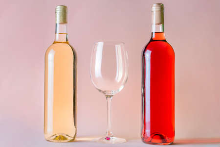 Two bottles of wine, one rosÃ© and the other white, with an empty glass between the two.の写真素材