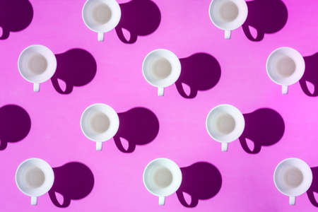 Pattern of coffee cups from a top view casting a hard shadow with the silhouette of another cup.