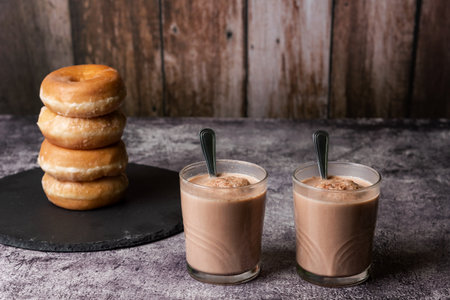 Two glasses of milk with cocoa with four glazed donuts on a stone plate.の写真素材