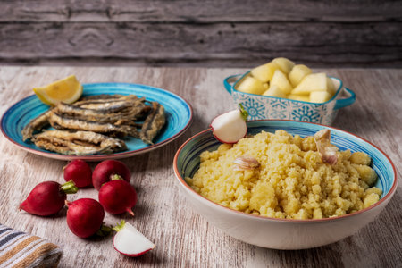 Plate of migas, traditional Spanish food, accompanied with radishes, fish and melon on a wooden table.の写真素材