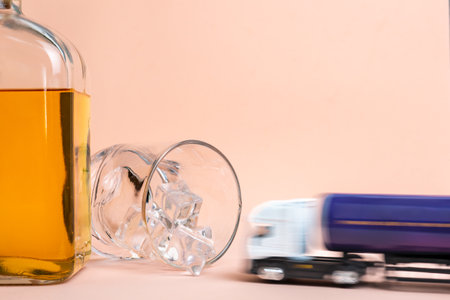 Whiskey bottle and glass lying with ice cubes, a toy tanker truck at high speed goes towards the glass to crash irretrievably.の写真素材