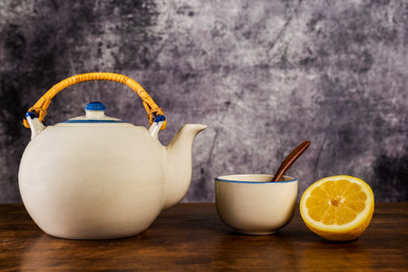 Porcelain teapot next to a cup for tea with a wooden spoon and half a lemon.の写真素材