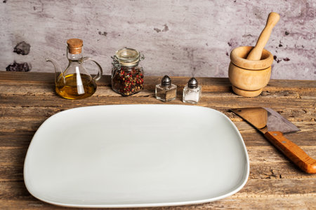 White empty rectangular plate next to salt, pepper, oil and a mortar on an old wooden table.の写真素材