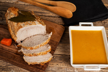 Piece of pork loin with beer cut into slices, next to a bowl with its sauce.の写真素材