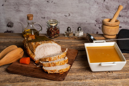 Piece of pork loin with beer cut into slices, decorated with bay leaves and carrot pieces, next to a bowl with its sauce.の写真素材