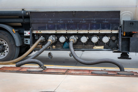 Fuel tanker unloading at a service station, with two hoses connected and another for gas recovery.の写真素材