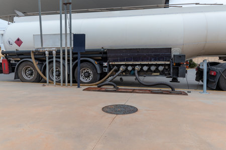 Fuel tanker truck unloading at a service station, with two hoses connected, gas recovery hose and ground connection.の写真素材
