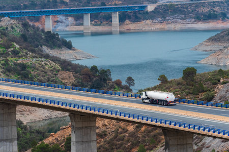 Tanker truck with dangerous goods plates driving through a viaduct over a swamp.の写真素材