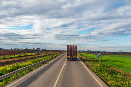 Truck with a container circulating on a conventional road next to cultivated fields.の写真素材