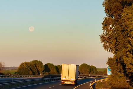Truck driving on a highway at dawn with the moon still visible.の写真素材