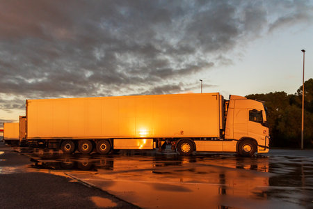 View of a truck with a refrigerated semi-trailer in a parking lot with the evening sun reflected on the side.の写真素材