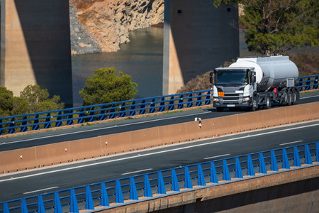 Fuel tanker truck driving on the highway with the pillars of a bridge behind. Side view.の写真素材