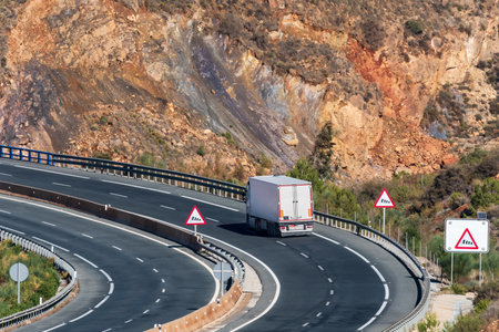 Truck with a refrigerated semi-trailer driving on a road with warning signs for strong winds.の写真素材