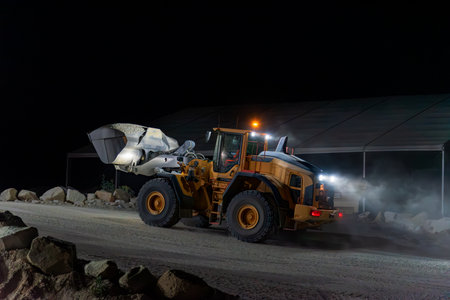 Heavy construction and mining machinery with a bucket full of sand, working the night shift. Close-up.の写真素材