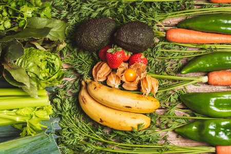 Background with dominant green stems of carrots, peppers, leeks, celery, lettuce, bay leaf, parsley, bananas, physalis, strawberries and avocado.の写真素材