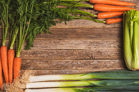 Background of old wooden boards with carrots with their green stem, leek and celery.の写真素材