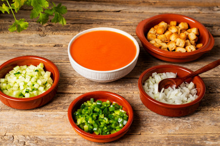 Bowl with gazpacho next to some clay plates with chopped vegetables and fried bread to add to the gazpacho.の写真素材