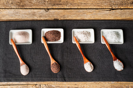 Wooden spoons next to some small plates with different types of salt, black, pink, flakes and seasoned with truffle.の写真素材