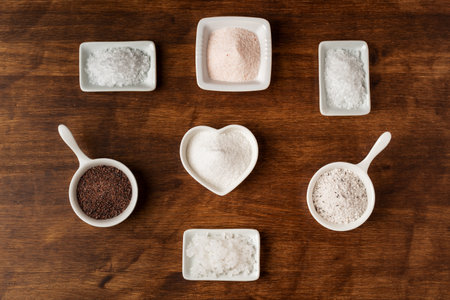 Small jars with different types of salt, black and pink from the Himalayas, normal, coarse, flakes, seasoned with truffle and from the Blackwater River (UK), on a wooden background.の写真素材