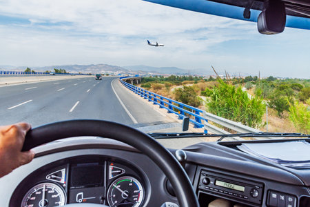 View from inside the cabin of a truck driving on a highway and a plane flying at low altitudeの写真素材