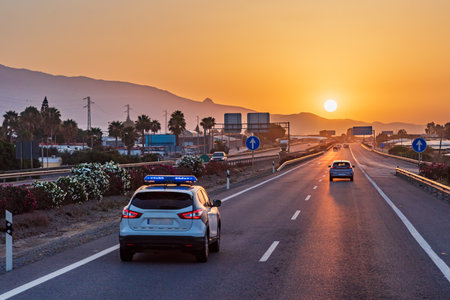 Traffic police car driving on a highway with the early morning sun rising over the mountains.の写真素材
