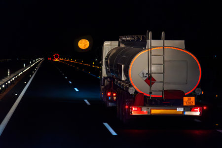Tanker truck with danger plates, transporting fuel, driving at night on the highway with the full moon in the background. Unretouched photography, a single shot.の写真素材
