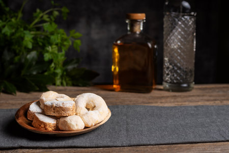 Shortbread, wine donuts and puff pastry on a wooden plate, and in the background and out of focus some bottles of anise and typical Christmas liqueur.の写真素材