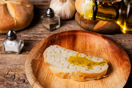 Bottle of olive oil pouring oil on a slice of bread, next to a shaker of salt, pepper, garlic and a piece of bread.の写真素材