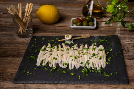 Black stone plate with some anchovies in vinegar and seasoned with garlic and parsley.の写真素材