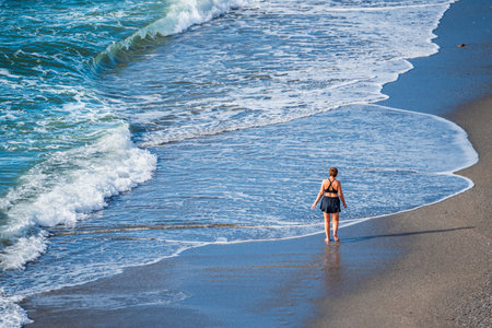 Woman walking on the sand of the beach barefoot at the height of the sea water.の写真素材