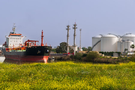 Liquid bulk merchant ship moored in a dock of a river port next to some huge warehouses.の写真素材