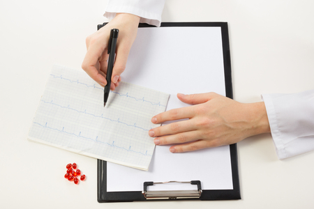 Healthcare and medicine concept - doctor with medical clipboard and red pills analyzing cardiogram. Top viewの写真素材