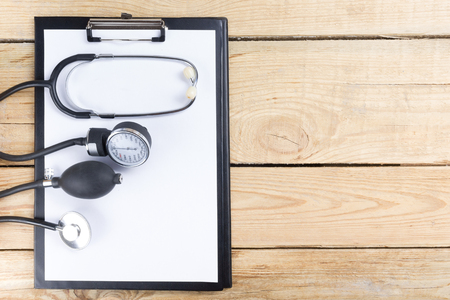 Medical clipboard and stethoscope on wooden desk background. Top view. Workplace of a doctorの写真素材