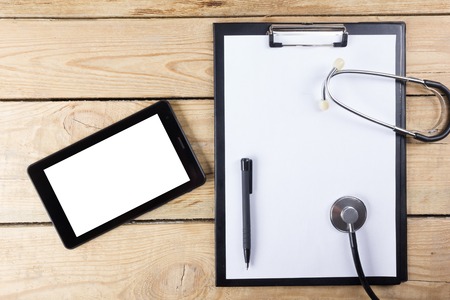 Medical clipboard and stethoscope on wooden desk background. Top view. Workplace of a doctorの写真素材