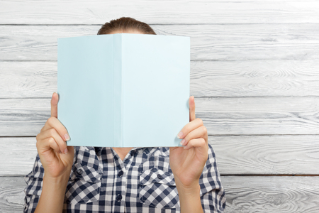 Woman reading a book and covering her face over wooden background.の写真素材