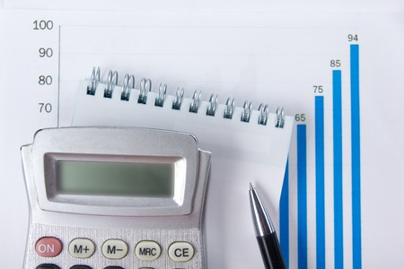 Finance concept - Financial accounting stock market graphs analysis. Calculator, notebook with blank sheet of paper, pen on chart. Top view.の写真素材