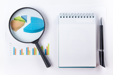 Finance concept - Financial accounting stock market graphs analysis. Magnifying glass, notebook with blank sheet of paper, pen on chart. Top view.の写真素材