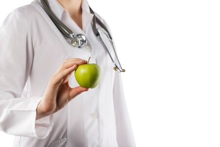 Female doctor's hand holding green apple. Close up shot on grey blurred background. Concept of Healthcare And Medicine. Copy spaceの写真素材