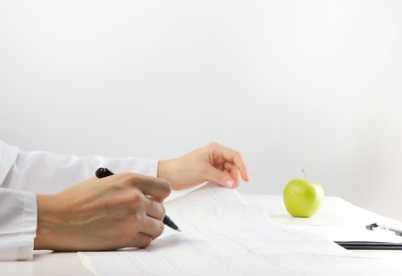 Healthcare and medicine concept - doctor with medical stethoscope and green apple analyzing cardiogram resultsの写真素材