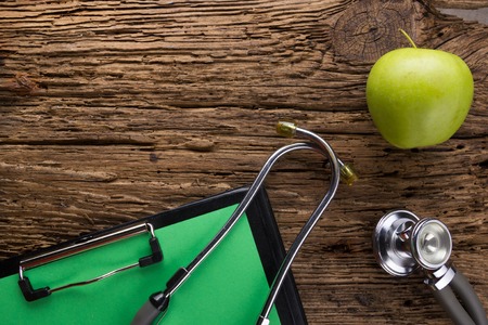 Alternative medicine - stethoscope, clipboard and green apple on wood table top view . Medical background. Concept for diet, healthcare, nutrition or medical insurance.