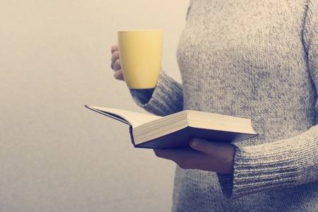 Young woman reading a book and holding cup of tea or coffee. Toned image.の写真素材