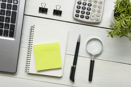 Office desk table with supplies and coffee cup. Top view. Copy space for text. Laptop, notepad, pen, magnifying glass, calculator, remindmer, flowerの写真素材