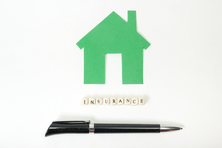 Concept of housing purchase and insurance. Office desk table with supplies top view - pen, green model house, wooden block with word Insuranceの写真素材