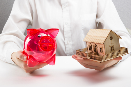 Mortgage and savings concept. hands holding money box and miniature houseの写真素材