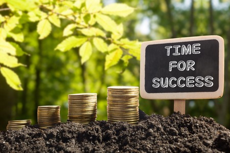 Time for success - Financial opportunity concept. Golden coins in soil Chalkboard on blurred natural backgroundの写真素材